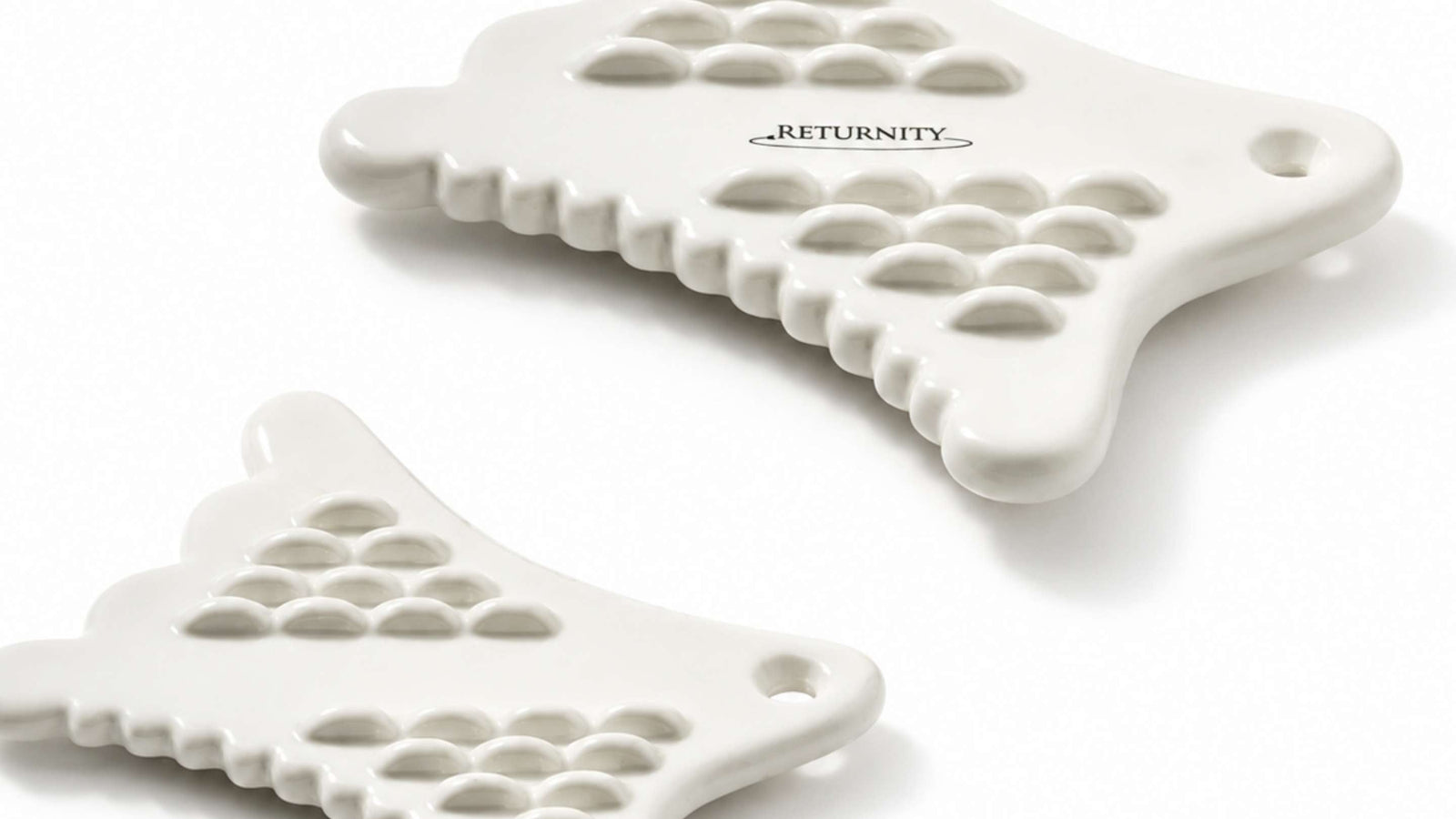 Tre vita Gua Sha-verktyg från Milk Touch placerade mot en ljusgrå bakgrund. Verktygen har en unik form med texturerade ytor och ergonomiska handtag, vilket ger en modern och stilren känsla. Skuggorna faller mjukt på ytan bakom dem.