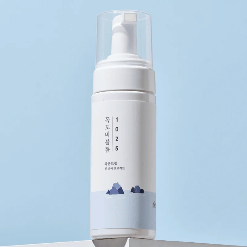  Produkt je "1025 Dokdo Bubble Foam" od ROUND LAB, zabalený v bielej pumpovacej fľaši s minimalistickým dizajnom. Je určený na hĺbkové čistenie tváre bez podráždenia.