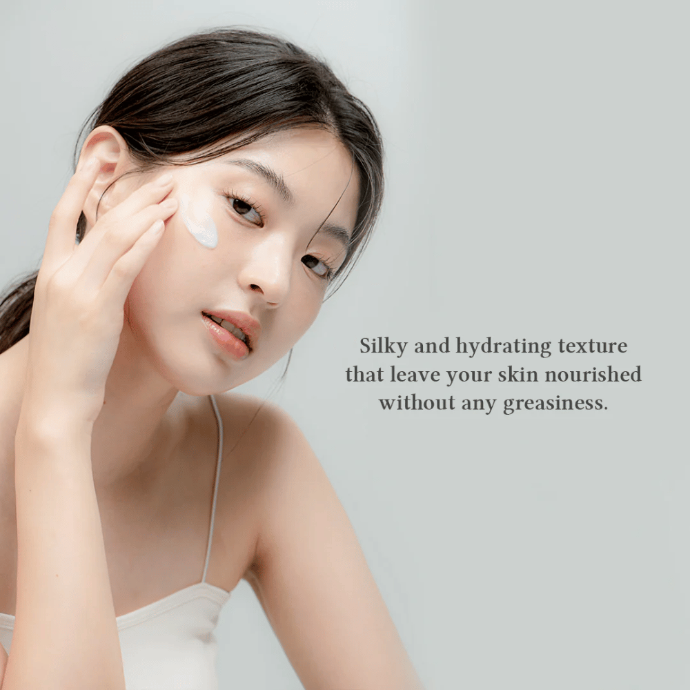 Obrázok ukazuje ženu, ktorá aplikuje krém na tvár. Text na obrázku popisuje produkt ako hodvábny a hydratačný, a zdôrazňuje, že vyživuje pokožku bez zanechania mastného pocitu. To naznačuje, že krém má ľahkú a príjemnú konzistenciu, ktorá sa dobre vstrebáva do pokožky.