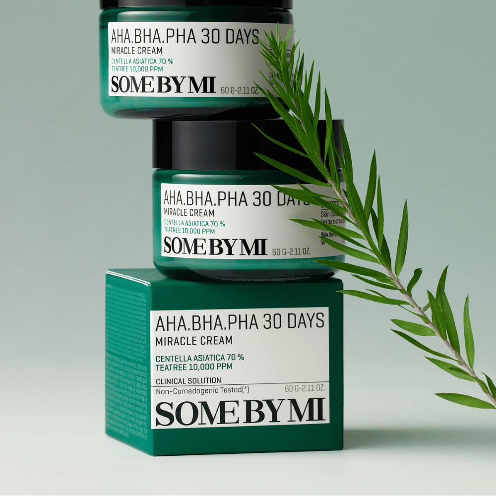 Obrázok ukazuje dve plechovky "SOME BY MI AHA, BHA, PHA 30 Days Miracle Cream" naskladané na zelenkavom pozadí. Krém, ktorý je bohatý na centella asiatica a tea tree olej, je navrhnutý na zlepšenie kvality pokožky a zmiernenie problémovej pokožky. Pôsobí hydratačne a upokojujúco.