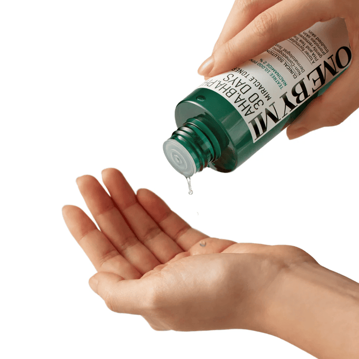 Ruka drží zelenú fľašu s nápisom "AHA, BHA, PHA 30 Days Miracle Toner" a vytláča číru tekutinu do dlane druhej ruky, pripravená na použitie.