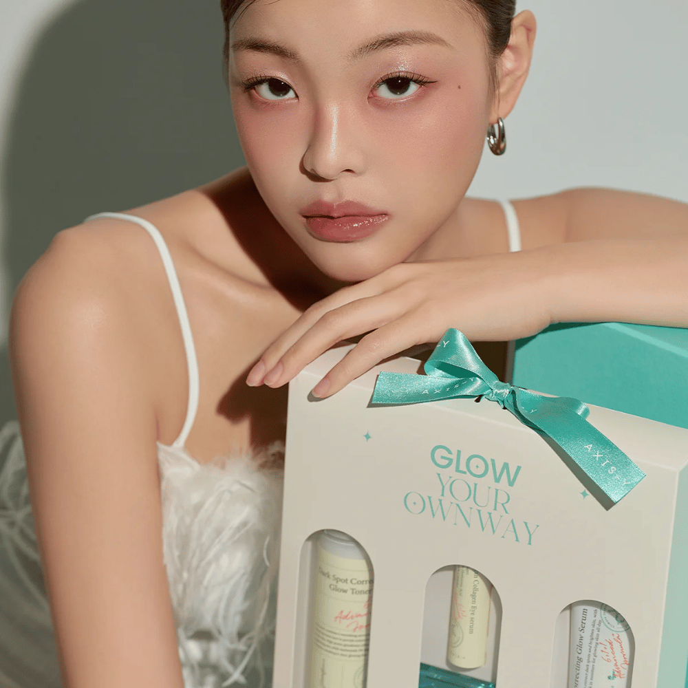 Modelka s elegantným make-upom drží darčekovú krabičku AXIS-Y „Glow Your Own Way“ – štýlovú súpravu starostlivosti o pleť, ideálnu ako darček pre seba alebo niekoho, koho máte radi.