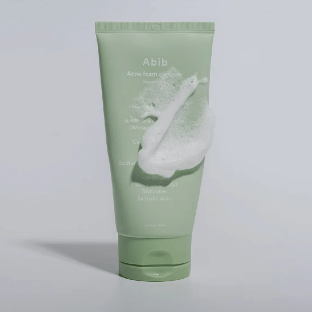Zelená tuba s Abib Acne Foam Cleanser Heartleaf, pokrytá bielou penou, ktorá ilustruje efekt penivého čistenia. Produkt obsahuje extrakt z listov srdca a kyselinu salicylovú pre pleť náchylnú na akné.