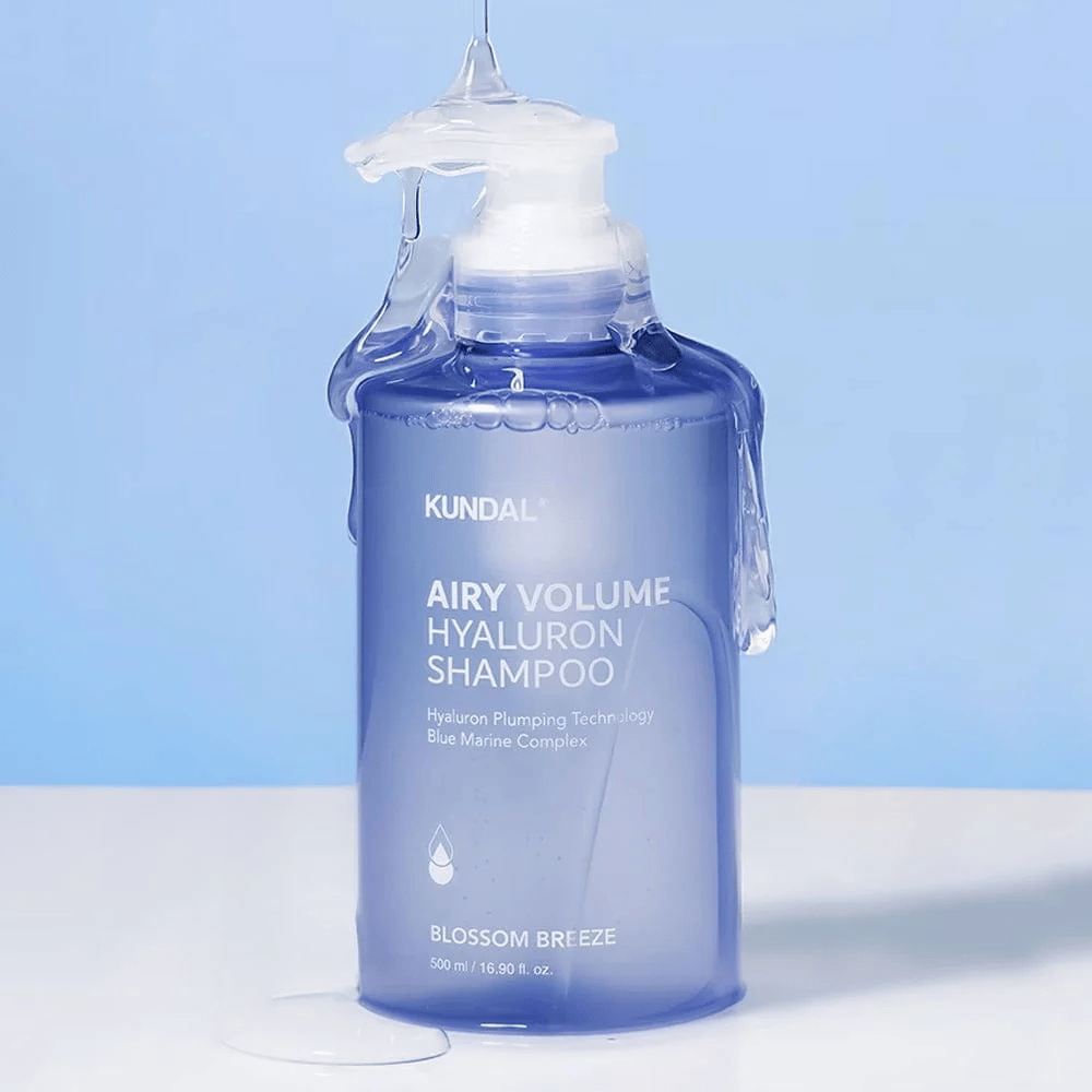 KUNDAL Airy Volume Hyaluron Shampoo Blossom Breeze v modrej pumpovacej fľaši, s kyselinou hyalurónovou a Blue Marine Complex, fotografovaný s tečúcou vodou.