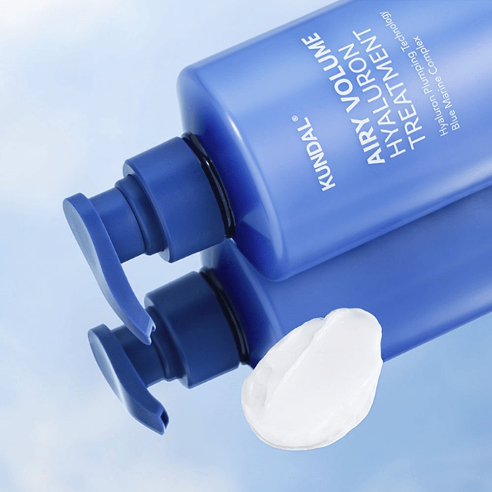KUNDAL Airy Volume Hyaluron Treatment v modrej pumpovacej fľaši ležiacej, s viditeľným bielym krémovým produktom vedľa.