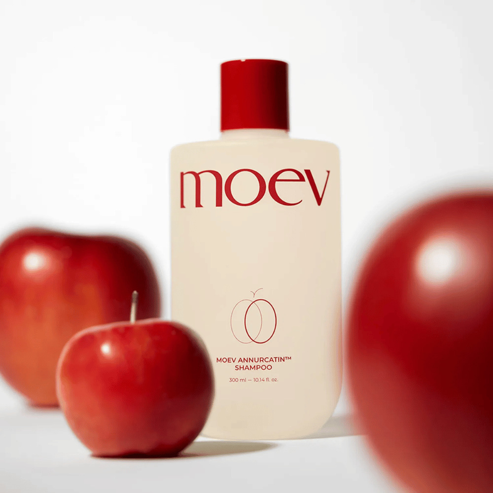 MOEV Annurcatin Shampoo umiestnený medzi červenými jablkami – inšpirovaný antioxidantmi Annurca-jablka, ktoré poskytujú silnejšie, zdravšie a lesklejšie vlasy.