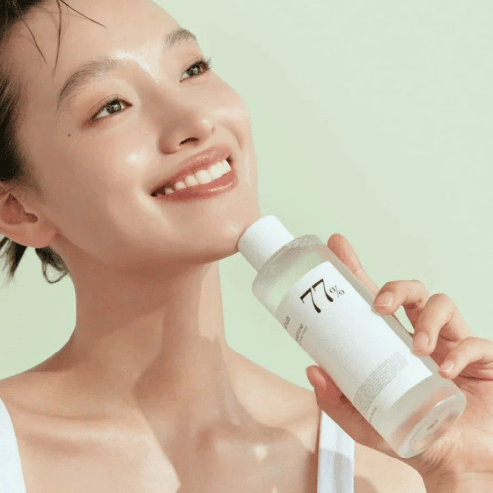 Žena upokojuje svoju citlivú pokožku fľašou Heartleaf 77% Soothing Toner od Anua, obsahujúcou extrakt z chameleónových listov.
