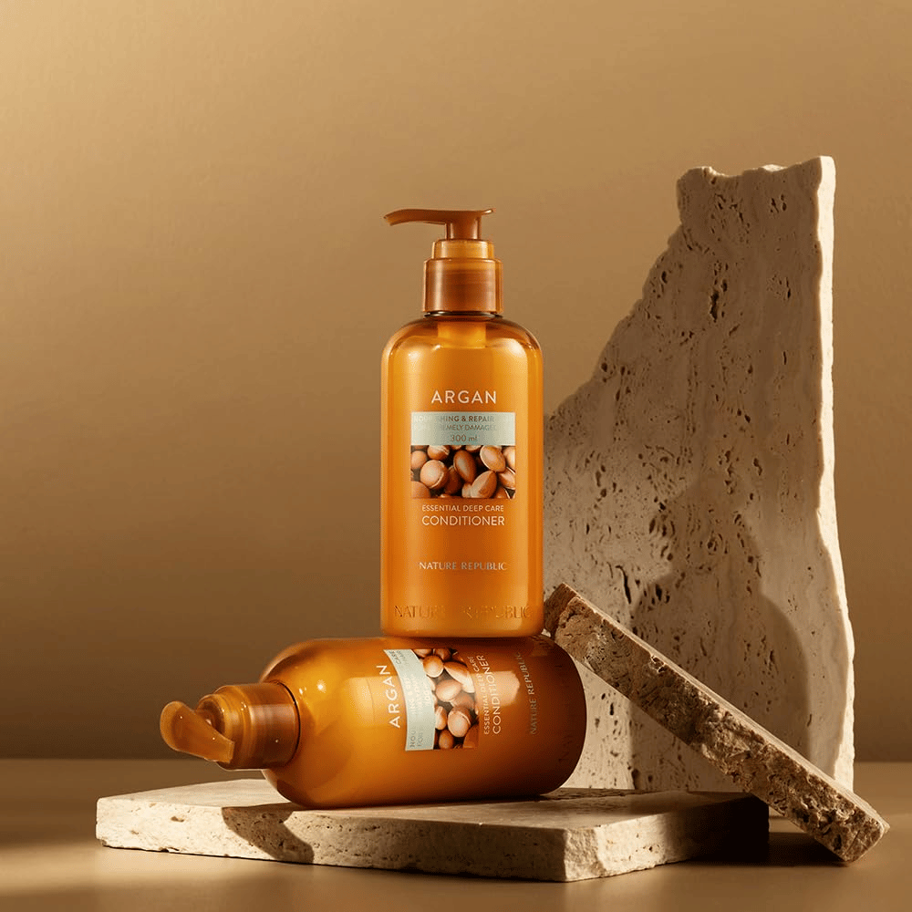 Dve fľaše Nature Republic Argan Essential Moisture Repairing Conditioner na kamennom povrchu v teplom tóne.