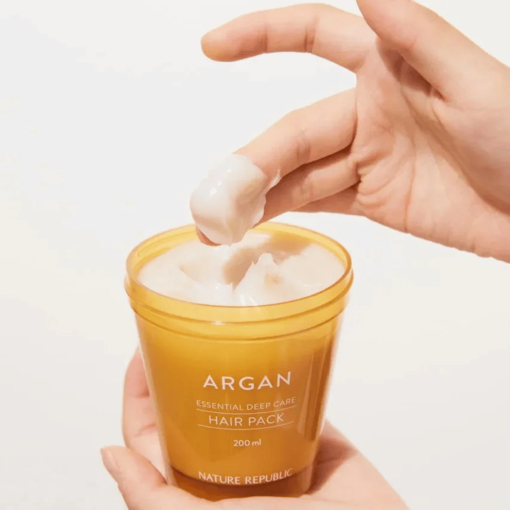 Ruka naberá krémovú formulu z Nature Republic Argan Essential Moisture Repairing Hair Mask – intenzívna výživa pre suché vlasy.