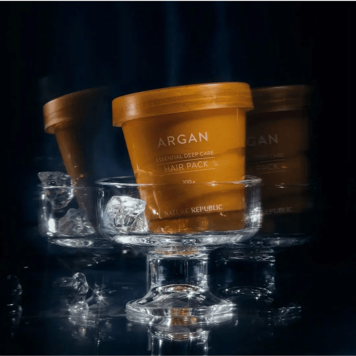 Nature Republic Argan Essential Moisture Repairing Hair Mask umiestnená na sklenenom tanieri s kockami ľadu – luxusná a ošetrujúca vlasová maska.