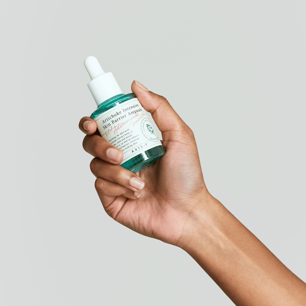 Ruka drží fľašu séra na starostlivosť o pleť s etiketou "Artichoke Intensive Skin Barrier Ampoule."