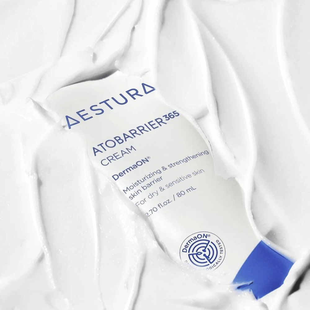 Aestura Atobarrier 365 Cream je perfektný pre suchú a citlivú pokožku. S technológiou DermaON™ tento krém hydratuje a posilňuje kožnú bariéru. Produkt je tu zobrazený v 80 ml tube, čiastočne pokrytý svojou vlastnou krémovou konzistenciou, čo zdôrazňuje jeho bohaté, hydratačné vlastnosti.