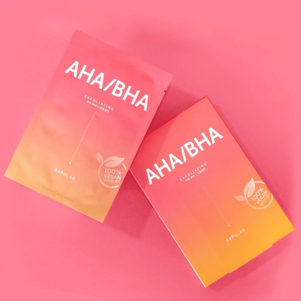 Dva produkty od BARULAB, jeden v sáčku a jeden v krabici, oba označené ako "AHA/BHA" a "Exfoliating" na ružovom pozadí. Produkty sú označené ako "100% vegánsky produkt".