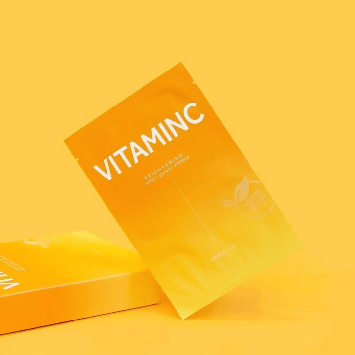 Kopa balení masiek BARULAB "VITAMINC Brightening", všetky označené ako "100% Vegan Product". Balenia majú farebný tón v rôznych odtieňoch oranžovej a žltej, umiestnené na jednotnom žltom pozadí.