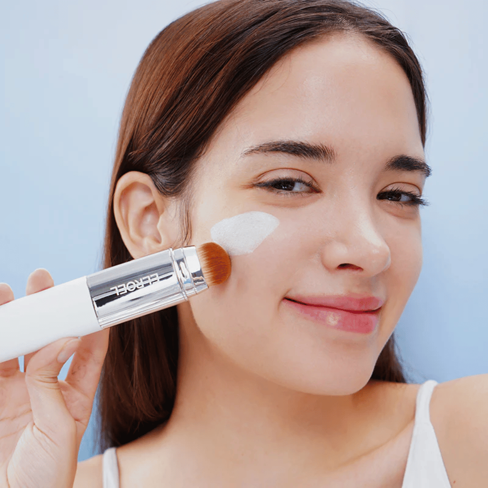 Model aplikuje ELROEL Blanc Cover Cream Stick concealer na líce s vstavaným štetcom pre prirodzené a rovnomerné krytie.