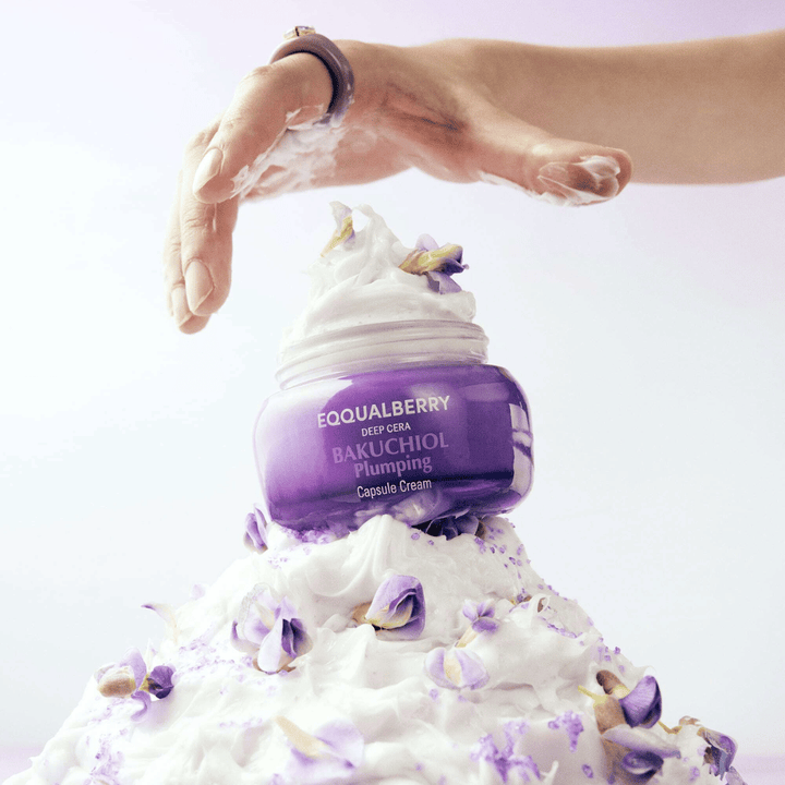EQQUALBERRY Bakuchiol Plumping Capsule Cream umiestnený na hromade šľahaného krému s kvetnými lístkami – symbolizuje hydratáciu a starostlivosť.