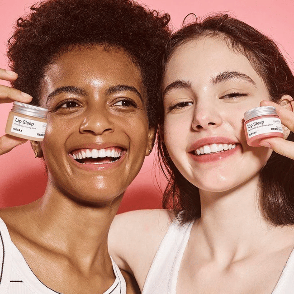 Dve osoby sa usmievajú a držia nádoby COSRX Lip Sleep. Obrázok vyjadruje jemné, hydratované pery a prirodzený žiariaci efekt produktu.