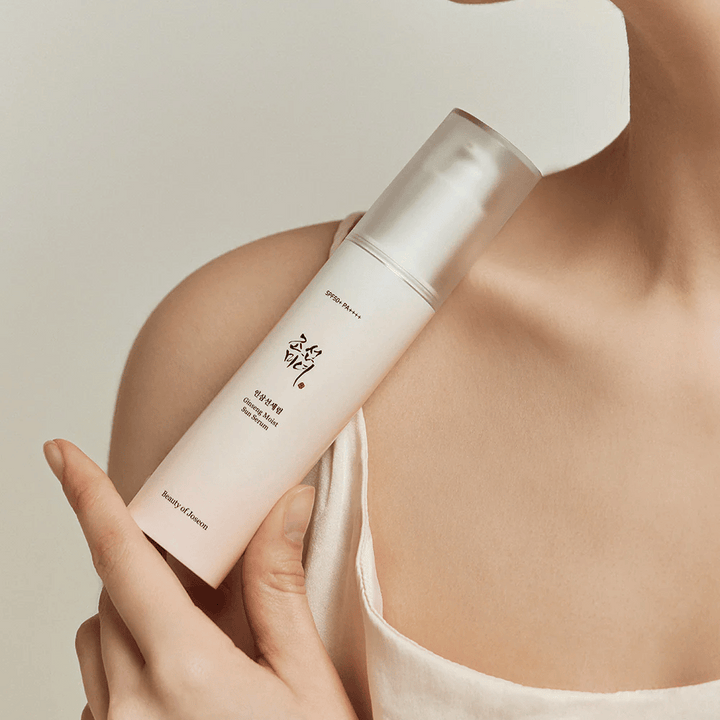 Žena, ktorá drží fľašu Beauty of Joseon's Ginseng Moist Sun Serum SPF 50+ PA++++, ktorá poskytuje ochranu SPF 50+ PA++++ a výhody starostlivosti o pleť.