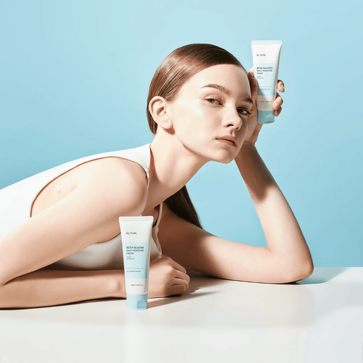 Lifestyle obrázok, na ktorom modelka pózuje s iUNIK Beta-Glucan Daily Moisture Cream na svetlomodrom pozadí. Obrázok sprostredkúva čistý, svieži a hydratačný dojem a zároveň jasne prezentuje produkt.