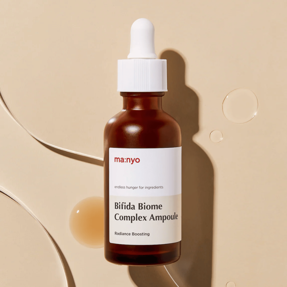Elegantný produktový obrázok ma:nyo Bifida Biome Complex Ampoule so zameraním na dizajn fľaštičky a kvapky séra v pozadí.