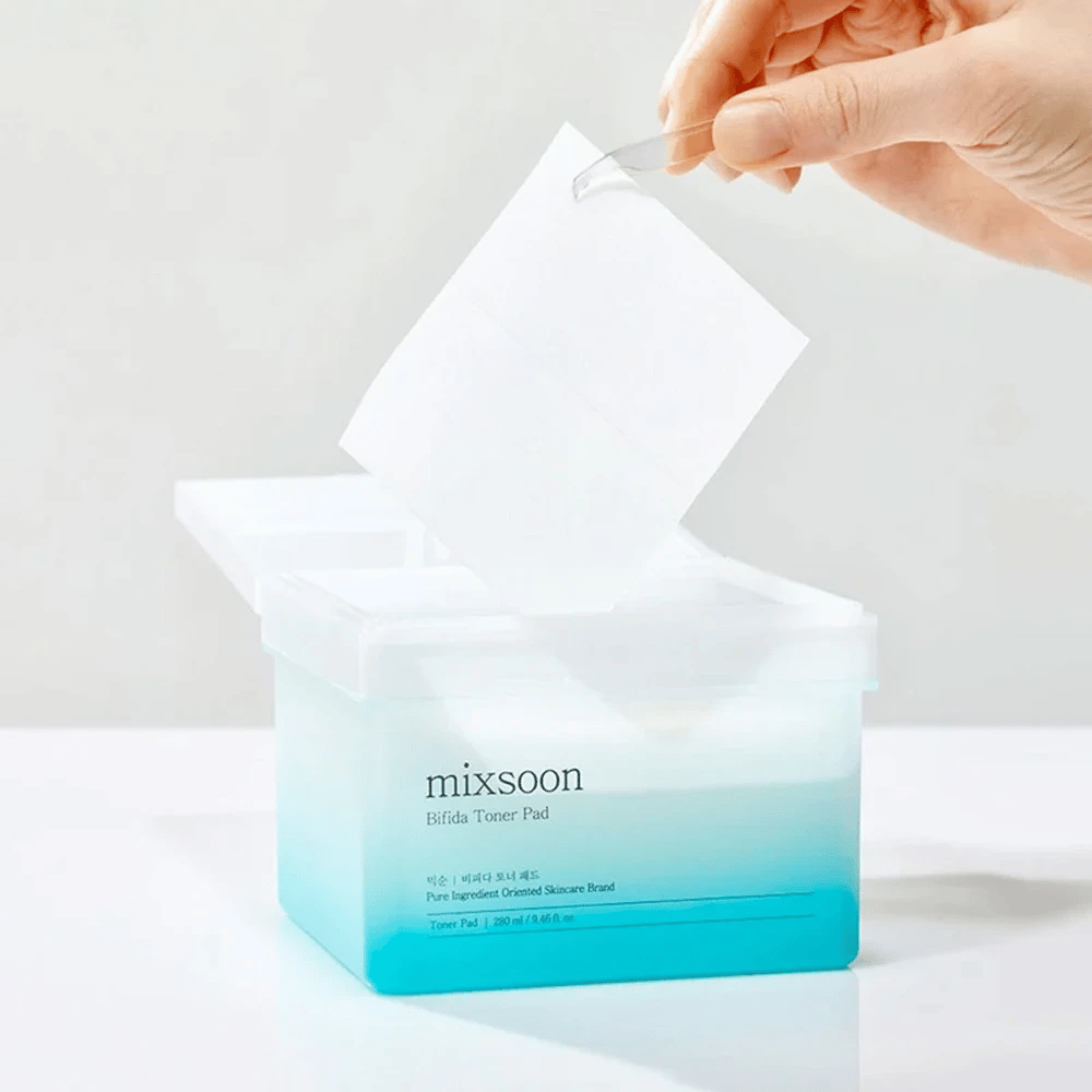 Priehľadná nádoba s modro-bielym prechodom obsahujúca Bifida tonerové podložky. Ruka vyberá tonerovú podložku z nádoby, ktorá je označená "mixsoon Bifida Toner Pad" a obsahuje 280 ml (9,46 fl. oz.) tonerových podložiek určených pre starostlivosť o pleť.