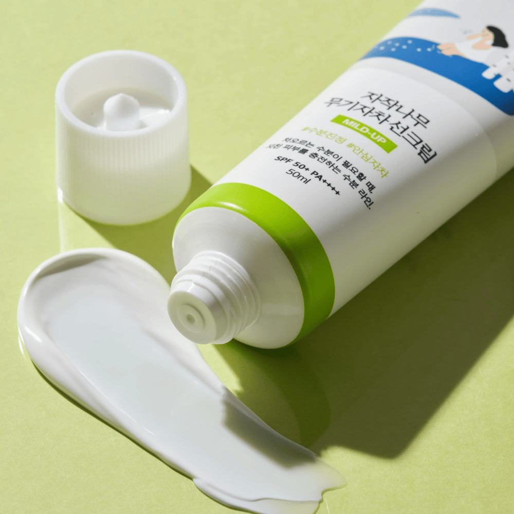 Záber na Birch Juice Moisturizing Mild Up Sunscreen s odskrutkovaným uzáverom, biely opaľovací krém rozmazaný na svetlozelenom pozadí, SPF 50+ PA++++, 50 ml.