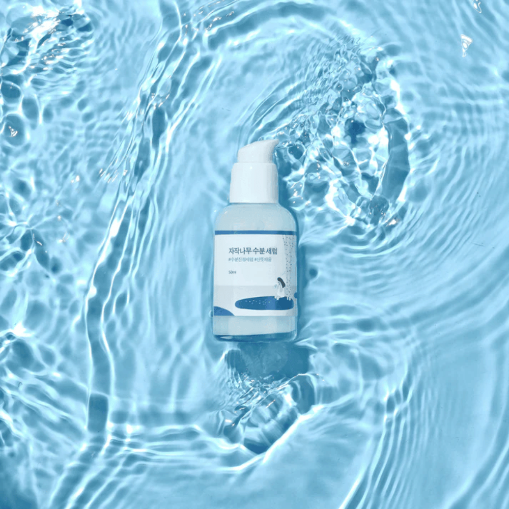 Round Lab Birch Juice Moisturizing Serum v pumpovacej fľaši plávajúcej na modrej vode s odrazmi slnečného svetla.