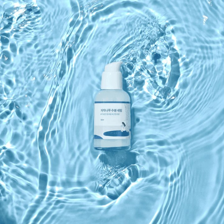 Round Lab Birch Juice Moisturizing Serum v pumpovacej fľaši plávajúcej na modrej vode s odrazmi slnečného svetla.