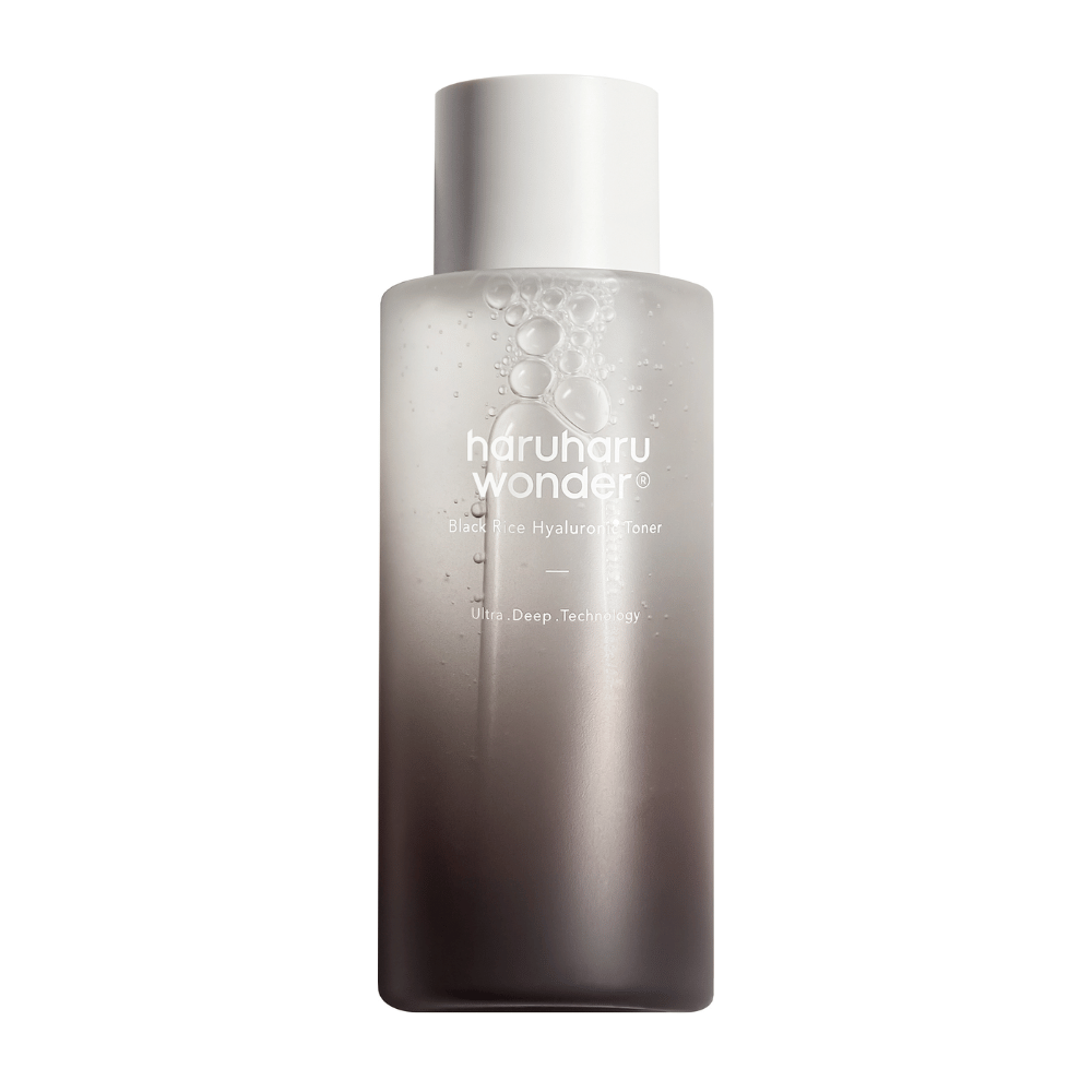 Fľaša haruharu wonder Black Rice Hyaluronic Toner s prechodom farieb od šedej po bielu a kvapkami vody na povrchu, na bielom pozadí.