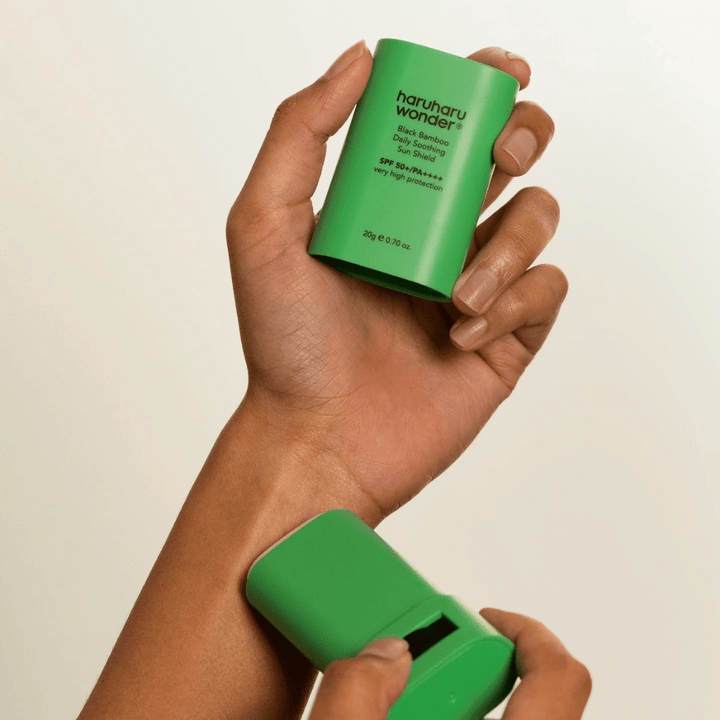 Osoba aplikuje Haruharu Wonder Black Bamboo Daily Soothing Sun Shield – zelený ochranný stick s SPF 50+ PA++++ – na zápästie.