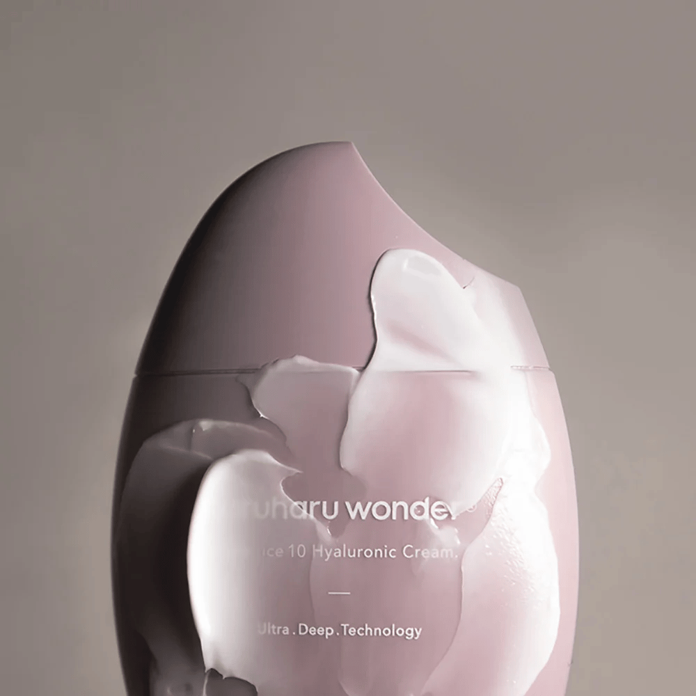 Obrázok ukazuje nádobu s "Haruharu Wonder Black Rice 10 Hyaluronic Cream", ktorá je čiastočne pokrytá hrubým, priehľadným krémom. Text na obrázku naznačuje použitie pokročilej technológie pre hlbokú hydratáciu pokožky. Dizajn je moderný a minimalistický.