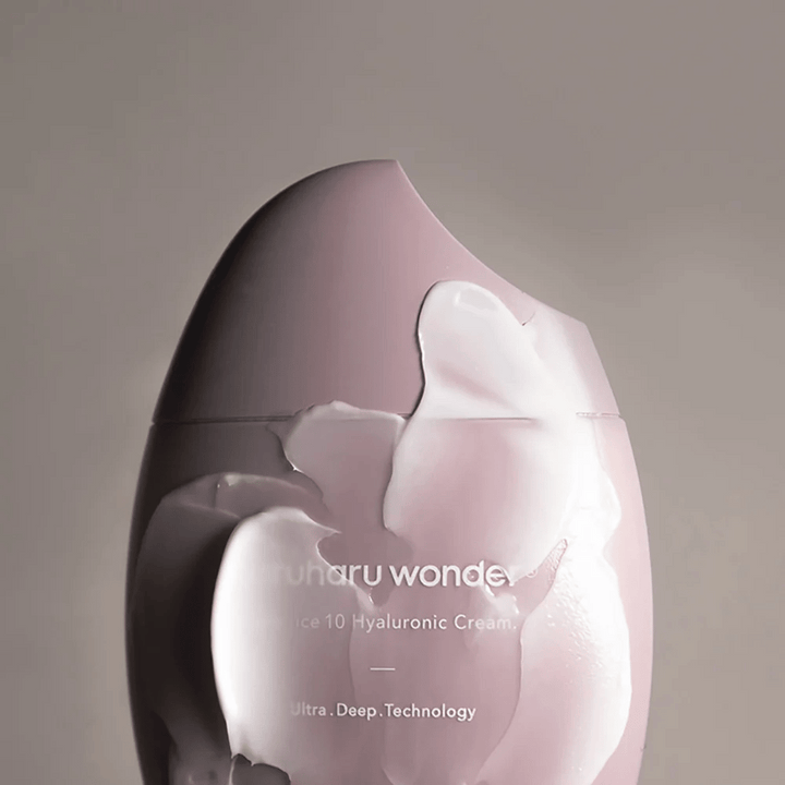 Obrázok ukazuje nádobu s "Haruharu Wonder Black Rice 10 Hyaluronic Cream", ktorá je čiastočne pokrytá hrubým, priehľadným krémom. Text na obrázku naznačuje použitie pokročilej technológie pre hlbokú hydratáciu pokožky. Dizajn je moderný a minimalistický.