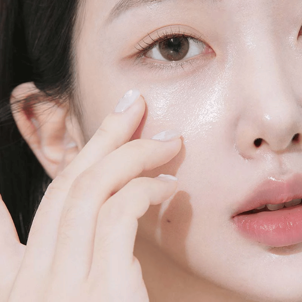 Detailný záber na ženu, ktorá nanáša očný krém pod oko pomocou končekov prstov. Pokožka vyzerá hydratovaná, lesklá a ošetrená s prirodzeným leskom.