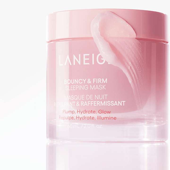 Detailný záber na Laneige Bouncy & Firm Sleeping Mask v ružovej nádobe, s časťou masky nanesenou na okraji viečka. Produkt je určený na to, aby poskytol vypnutie, hydratáciu a žiarivosť. Nádoba obsahuje 60 ml a má text "Vypnúť, Hydratovať, Žiariť."