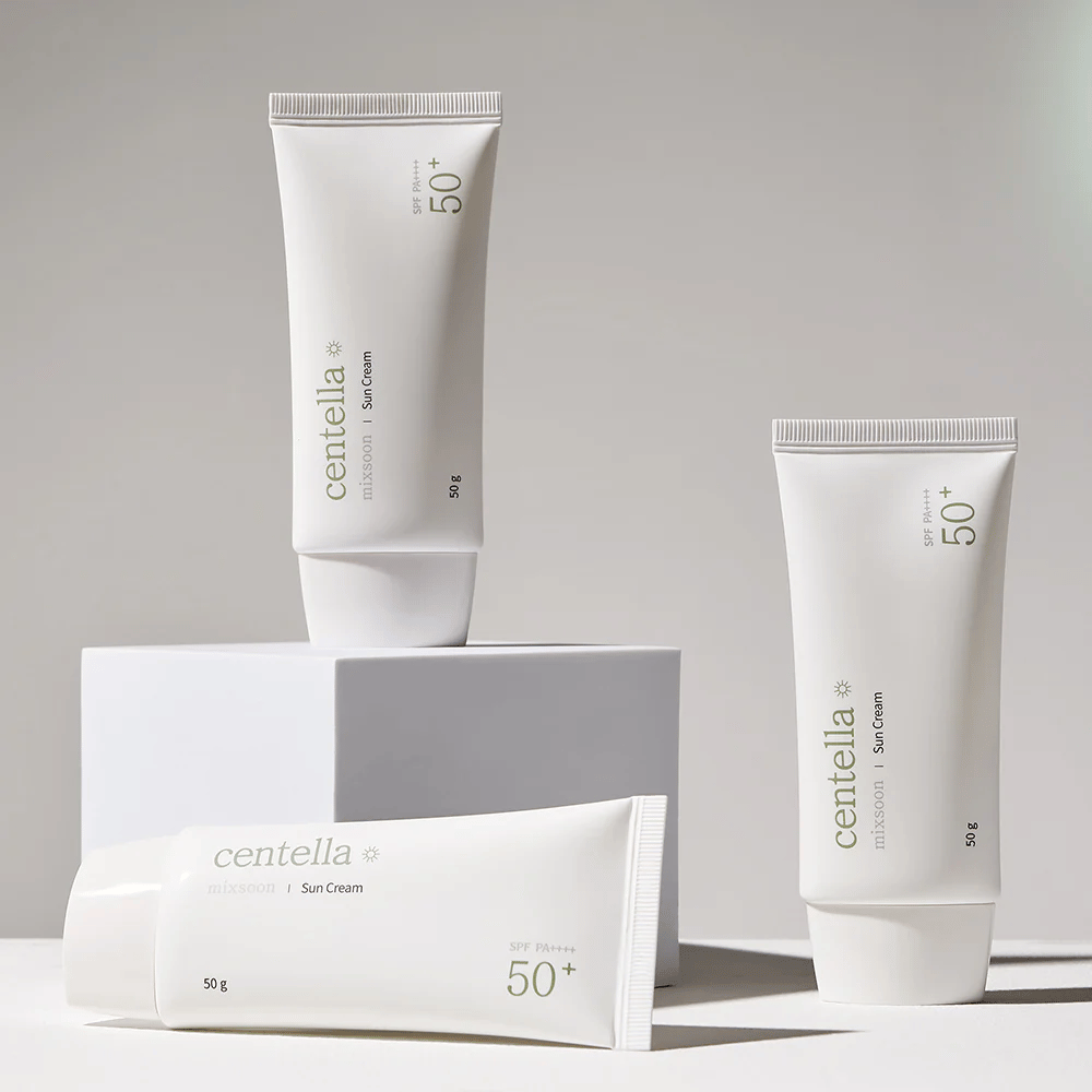 Tri balenia Centella Sun Cream SPF 50+ PA++++ usporiadané esteticky na bielych pódiách. Dve tuby stoja a jedna leží, všetky s bielym, minimalistickým dizajnom a zelenými textovými detailmi.