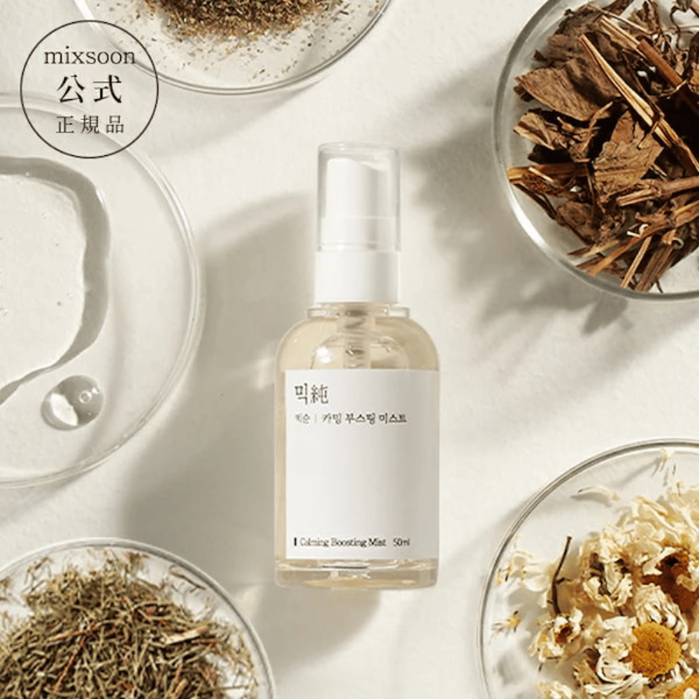 Priehľadná sprejová fľaša s etiketou 'Calming Boosting Mist' od Mixsoon, obklopená sušenými bylinkami a kvetmi na bielych miskách na béžovom pozadí, čo zdôrazňuje prírodné zložky produktov.