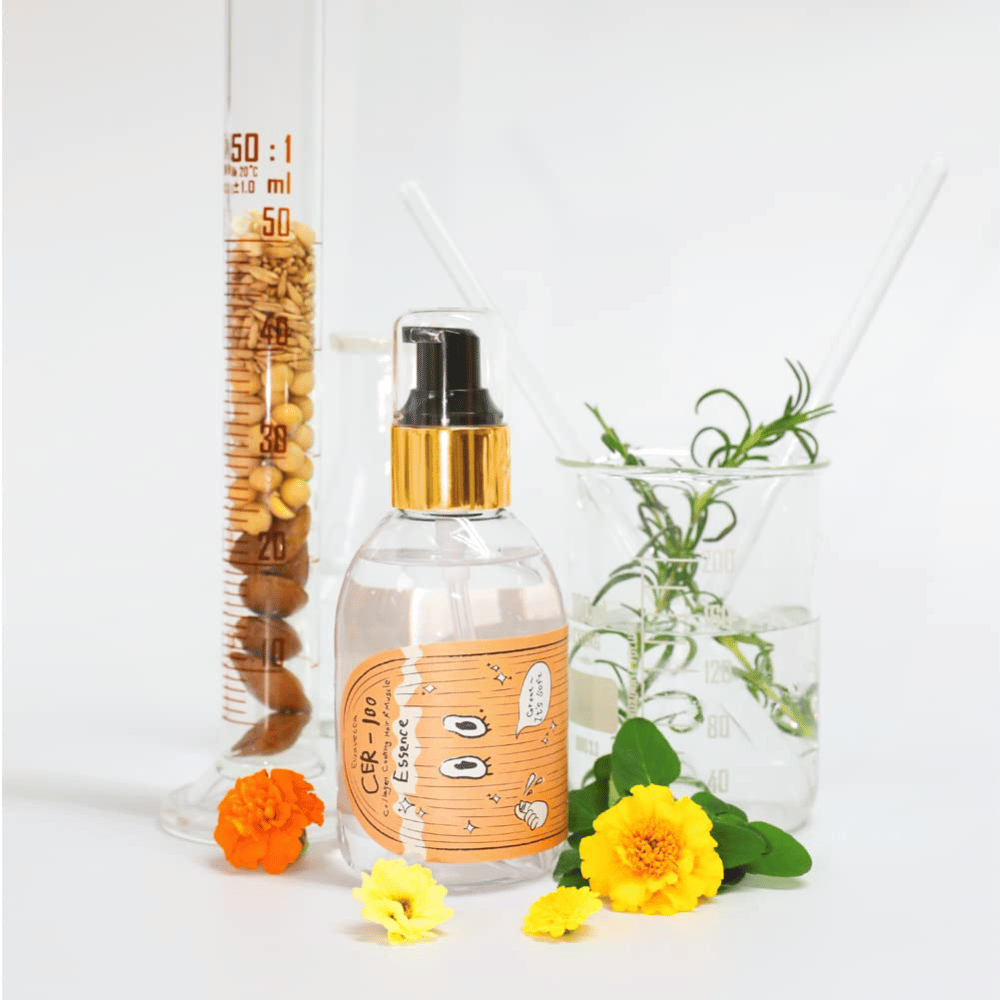 CER-100 Hair Essence spolu s kvetmi a laboratórnym sklom, ktoré zvýrazňujú ingrediencie a starostlivosť o vlasy.
