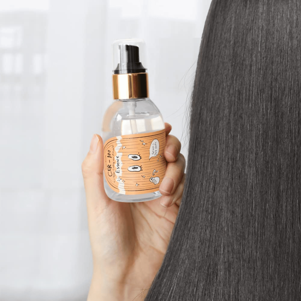 Osoba drží CER-100 Hair Essence vedľa dlhých, lesklých vlasov, aby ukázala jemnosť a starostlivosť.