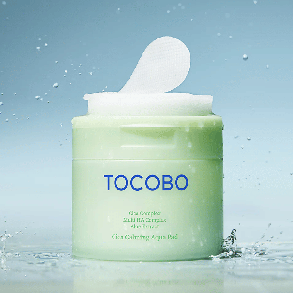 Otvorená dóza s TOCOBO Cica Calming Aqua Pad, kde z balenia vytŕča toner pad. Kvapky vody okolo produktu zosilňujú pocit intenzívnej hydratácie a sviežosti.