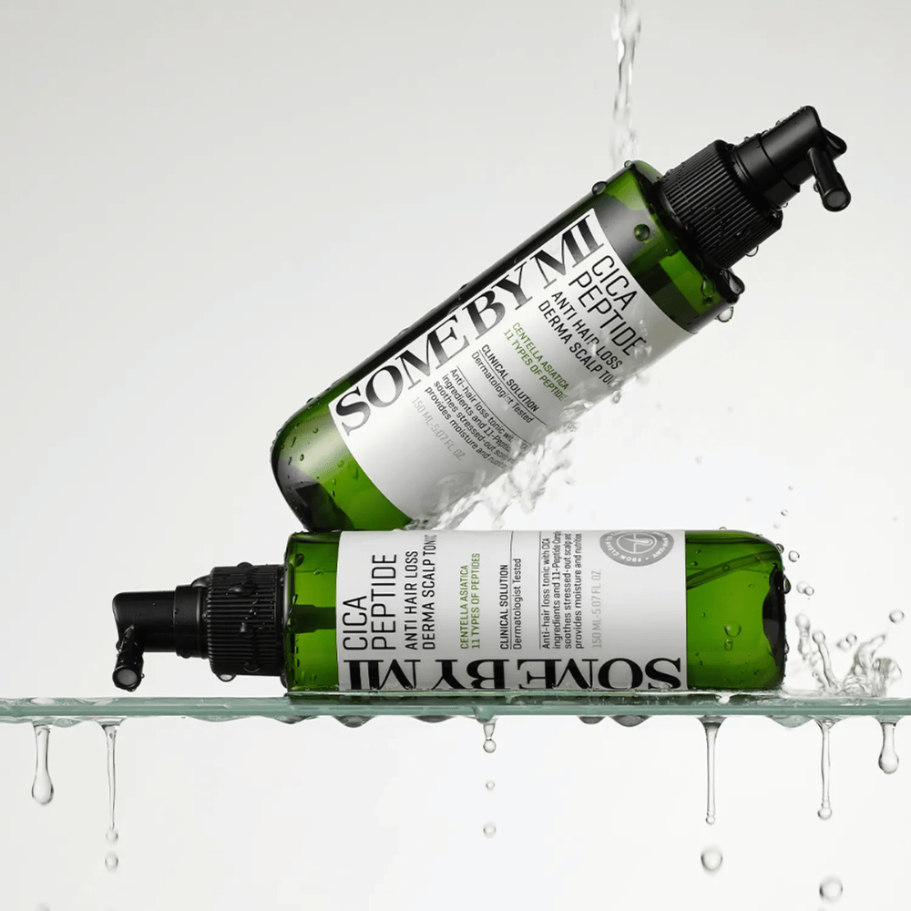 Dve fľaše SOME BY MI Cica Peptide Anti Hair Loss Derma Scalp Tonic ležia vo vode a nad vodou s kvapkami, ktoré špliechajú, zelené fľaše s čiernou rozprašovacou tryskou a bielou etiketou.