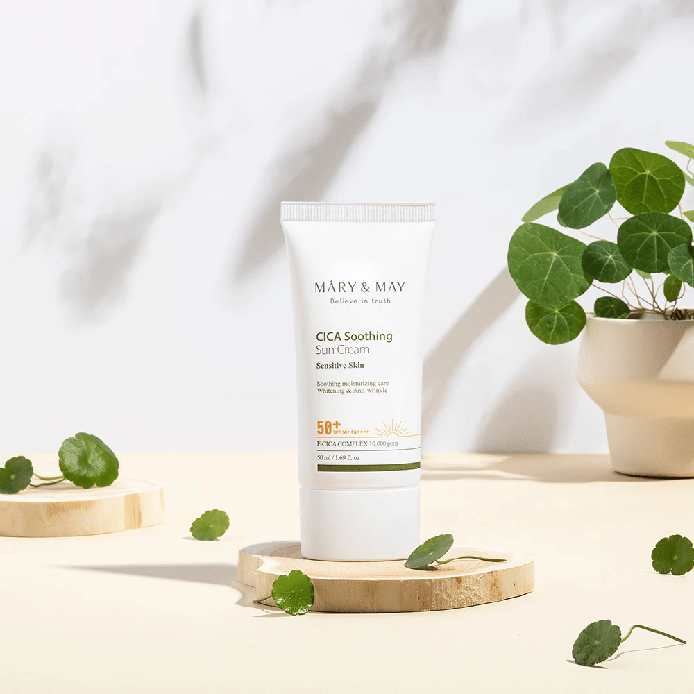 Mary&May CICA Soothing Sun Cream umiestnený na drevenom podstavci so zelenými listami centelly okolo. Obrázok zdôrazňuje zložky upokojujúce pokožku a prírodnú inšpiráciu produktu.