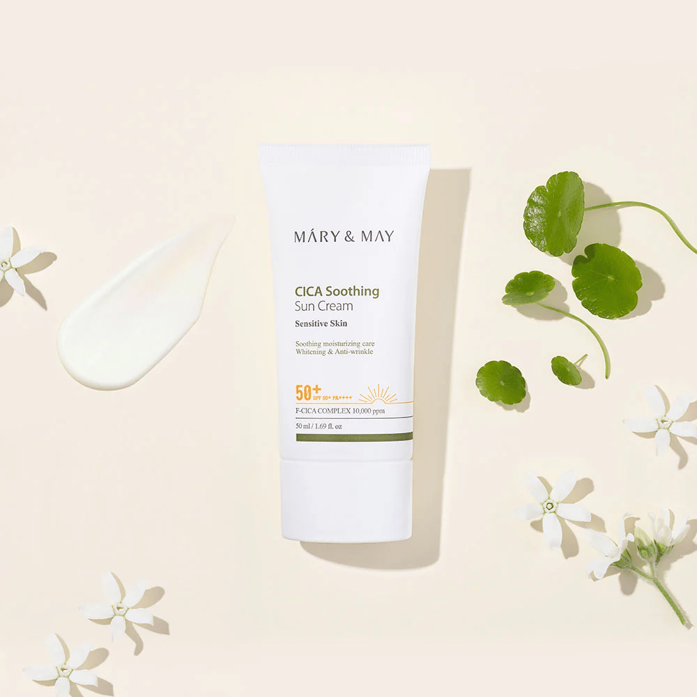 Mary&May CICA Soothing Sun Cream SPF50+ PA++++ prezentovaný spolu s krémovou textúrou, listami centelly a bielymi kvetmi. Obrázok zdôrazňuje upokojujúce vlastnosti produktu a zameranie na citlivú pokožku.
