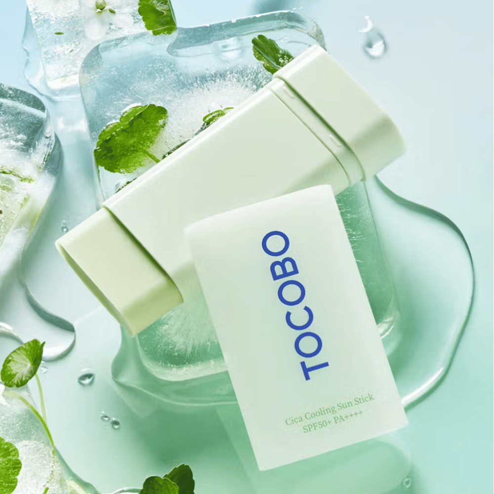 Tocobo Cica Cooling Sun Stick SPF50+ PA++++ na kockách ľadu so zelenými rastlinnými listami, čo sprostredkováva chladivý a osviežujúci pocit.