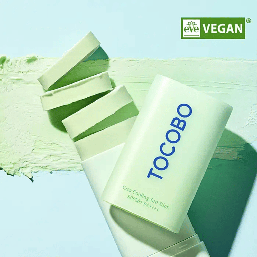 Tocobo Cica Cooling Sun Stick SPF50+ PA++++ v svetlozelenej škatuľke s vegánskym označením (EVE VEGAN), ležiace na vrstve zeleného opaľovacieho krému.