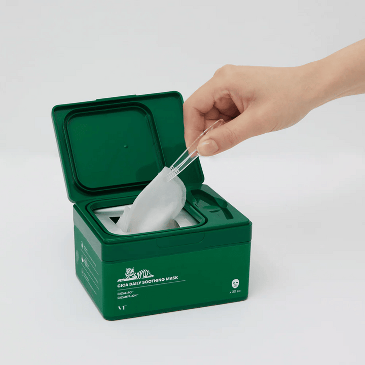 Ruka používa pinzetu na vybratie pleťovej masky zo zelenej nádoby označenej "Cica Daily Soothing Mask".