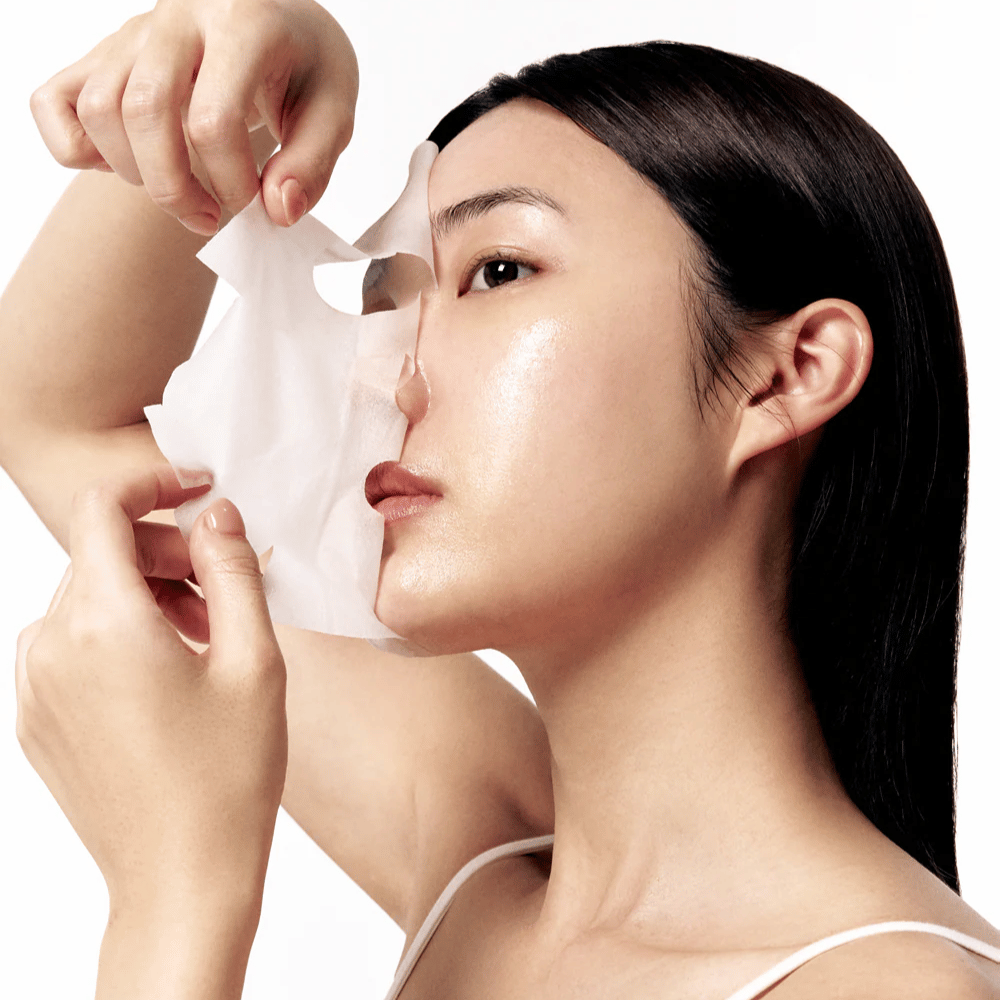 Žena s hladkou, hydratovanou pokožkou si sníma bielu pleťovú masku z tváre, čo odhaľuje žiarivý a rovnomerný tón pleti.