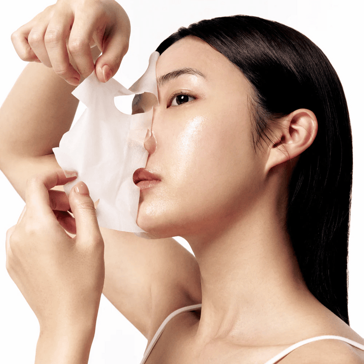 Žena s hladkou, hydratovanou pokožkou si sníma bielu pleťovú masku z tváre, čo odhaľuje žiarivý a rovnomerný tón pleti.