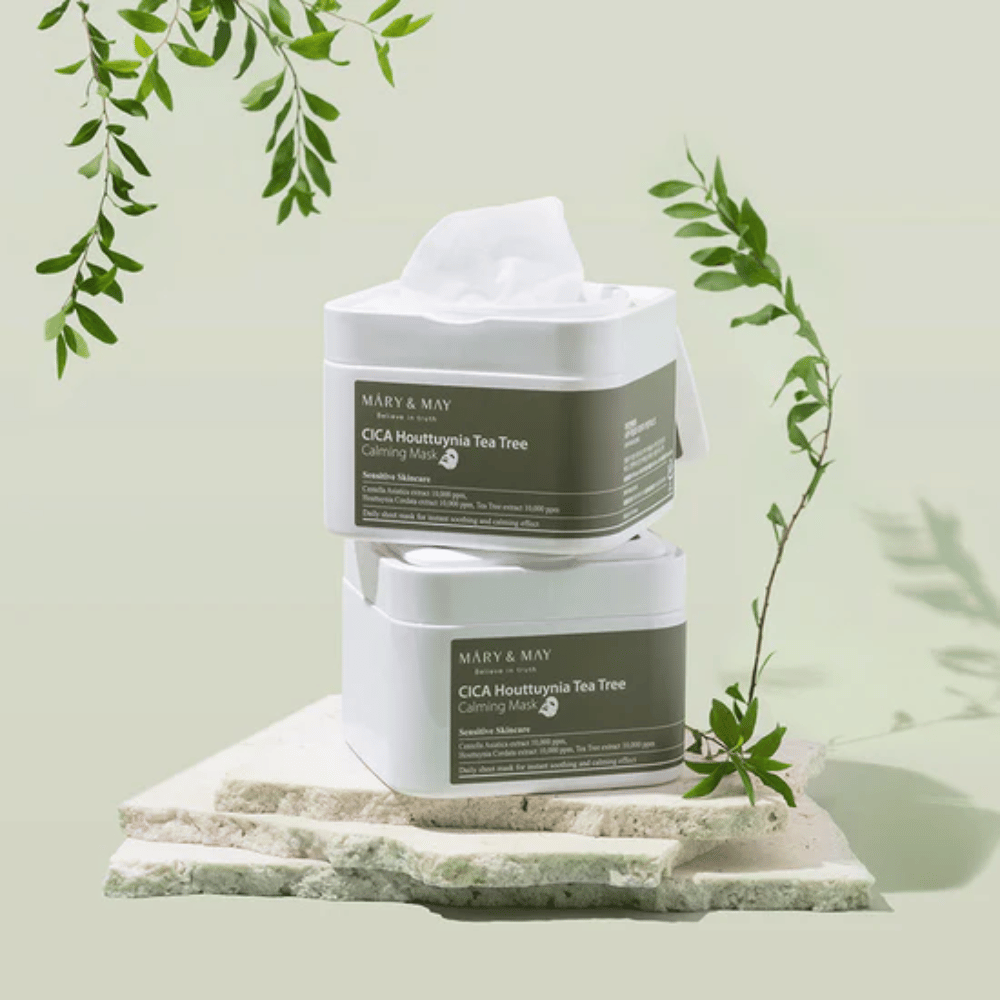 Dve nádoby Mary & May Cica Houttuynia Tea Tree Calming Mask umiestnené na prírodnom kameni so zelenými rastlinnými detailmi – upokojujúce pleťové masky pre citlivú pokožku.