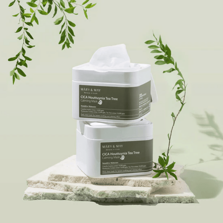 Dve nádoby Mary & May Cica Houttuynia Tea Tree Calming Mask umiestnené na prírodnom kameni so zelenými rastlinnými detailmi – upokojujúce pleťové masky pre citlivú pokožku.