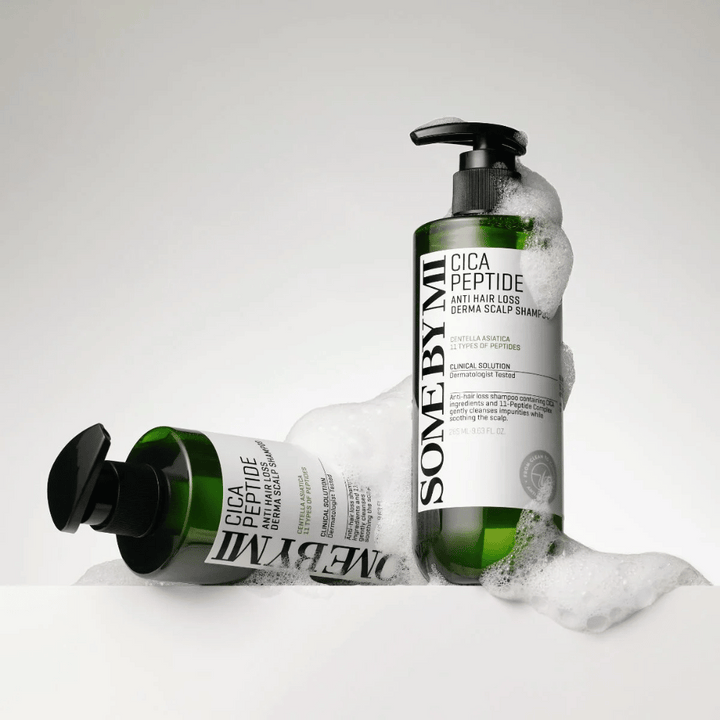 Dve fľaše SOME BY MI Cica Peptide Anti Hair Loss Derma Scalp Shampoo pokryté penou, stojace a ležiace na bielom pozadí.